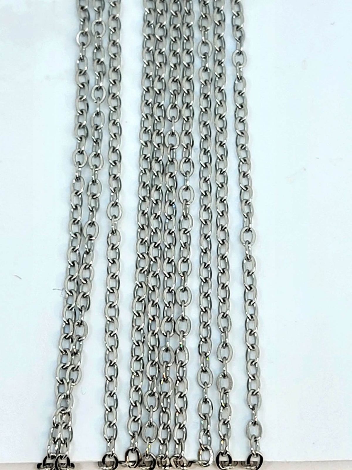 Hanging strands of 1.5mm rhodium stainless steel link chain against a white background
