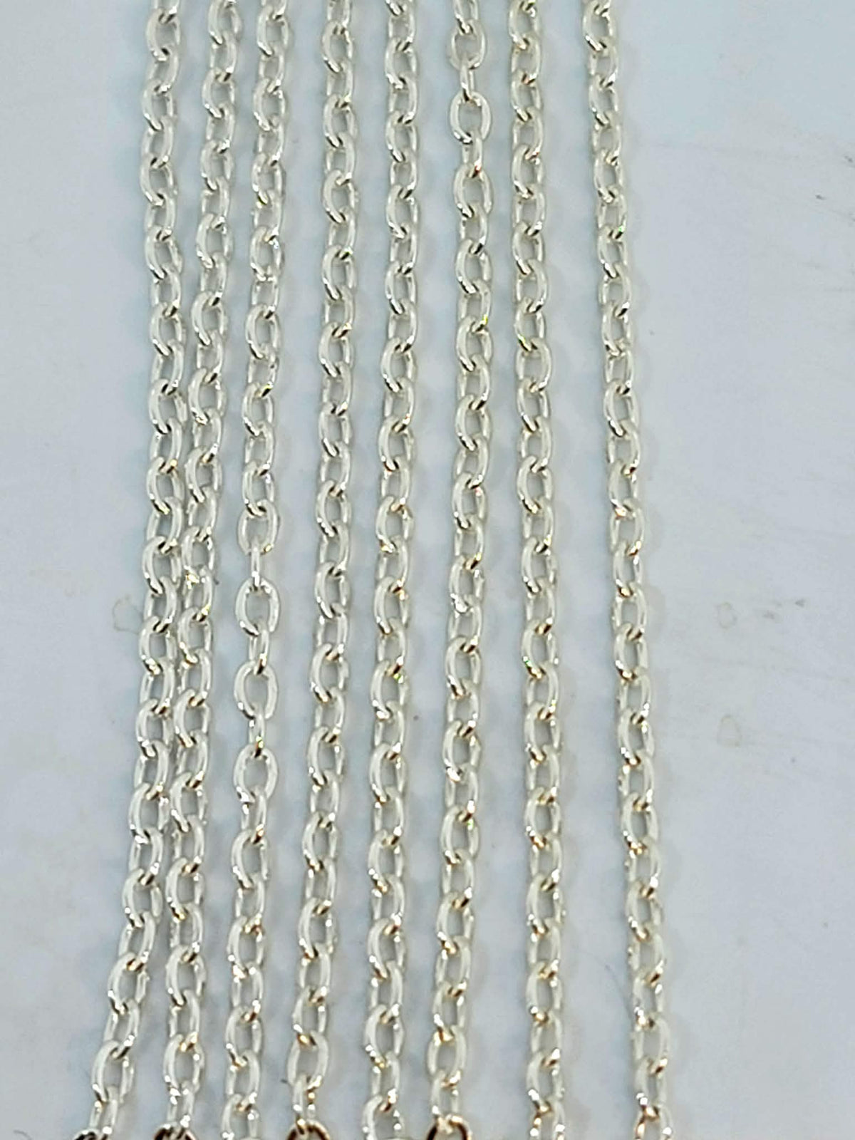Hanging strands of 1.5mm silver stainless steel link chain against a white background