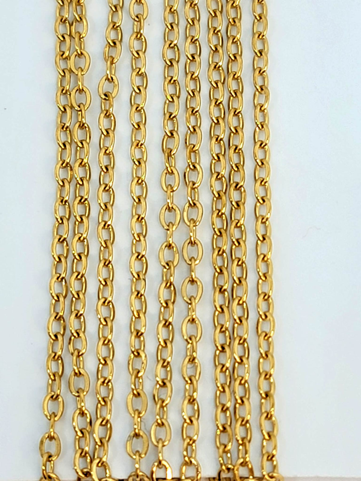 Hanging strands of 1.5mm gold stainless steel link chain against a white background