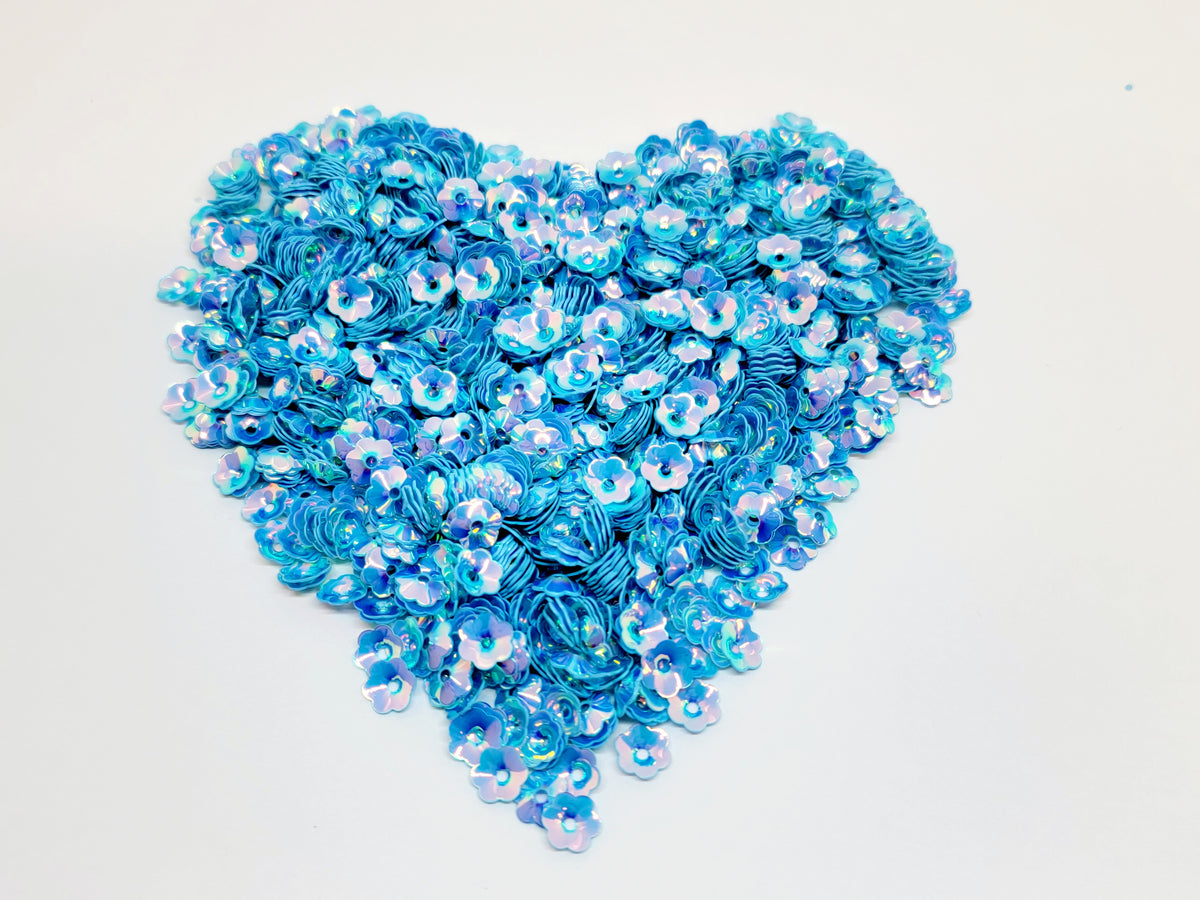 Heart-shaped pile of 6mm iridescent flower sequins in blue on a white background