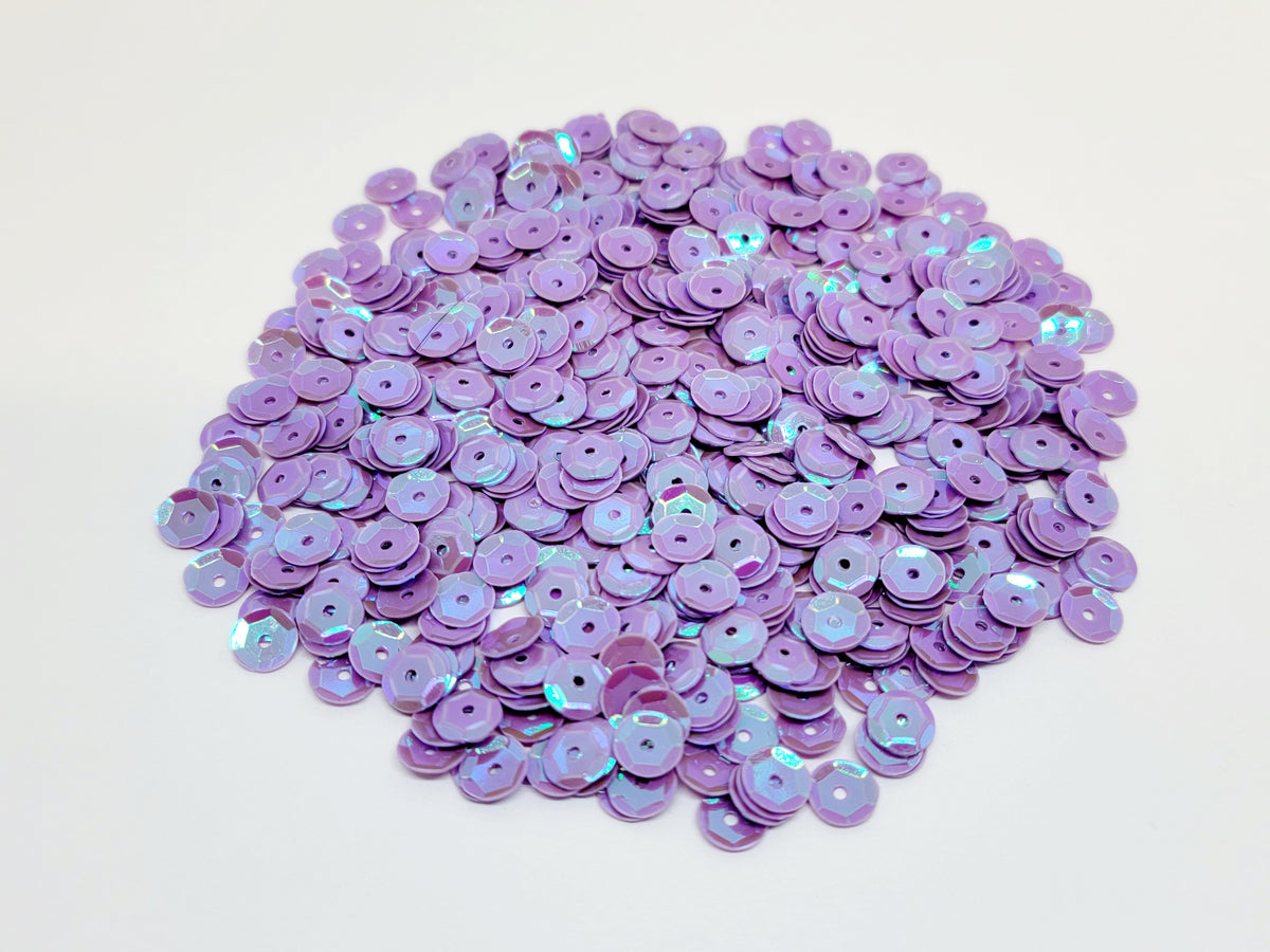 Pile of 6mm round purple sequins with centre holes, on a white background