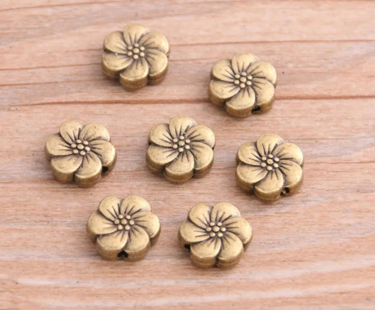 Bronze-tone 10 x 11mm flower spacer beads with white enamel petals on wood