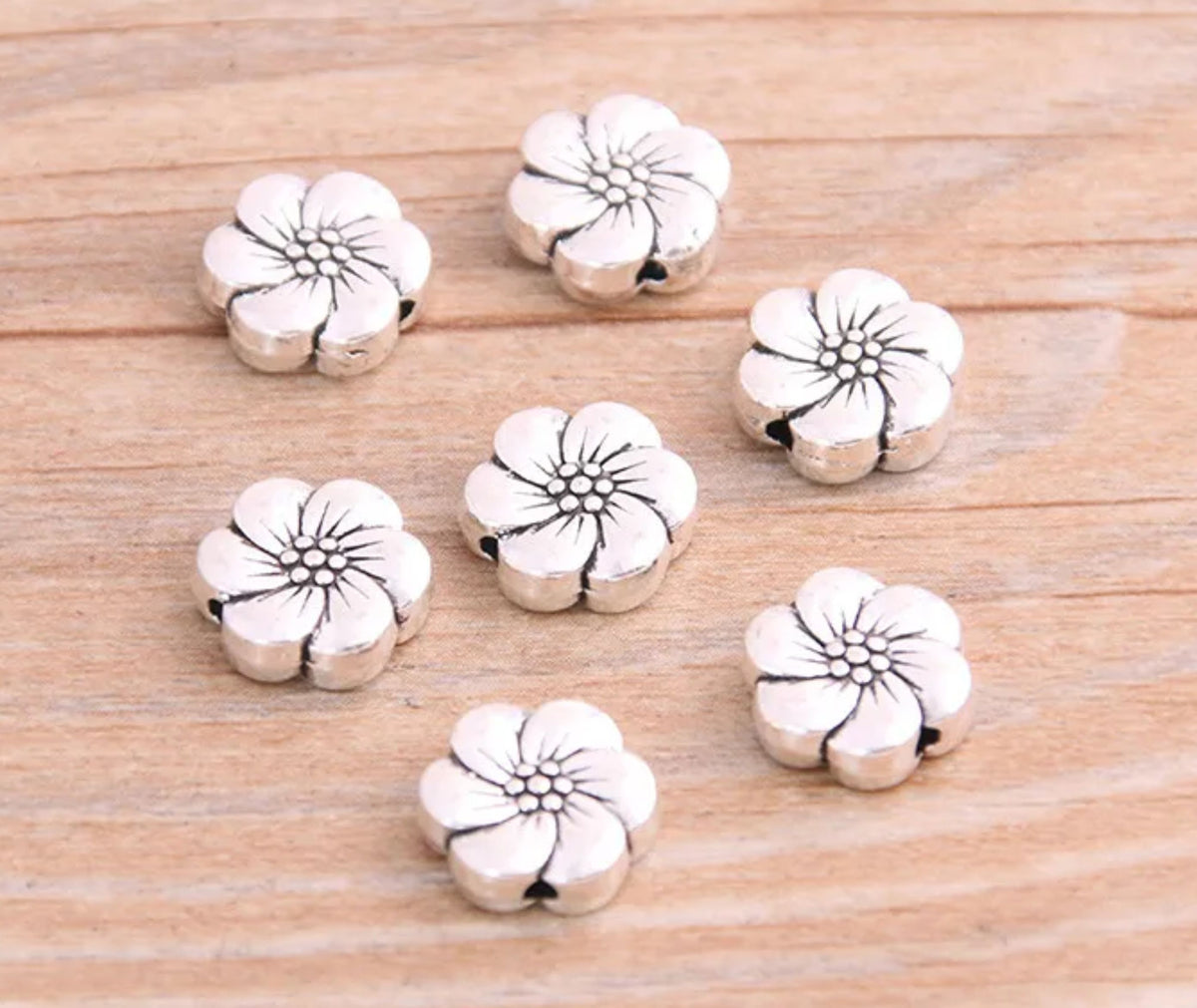 Silver-tone 10 x 11mm flower spacer beads with white enamel petals on wood