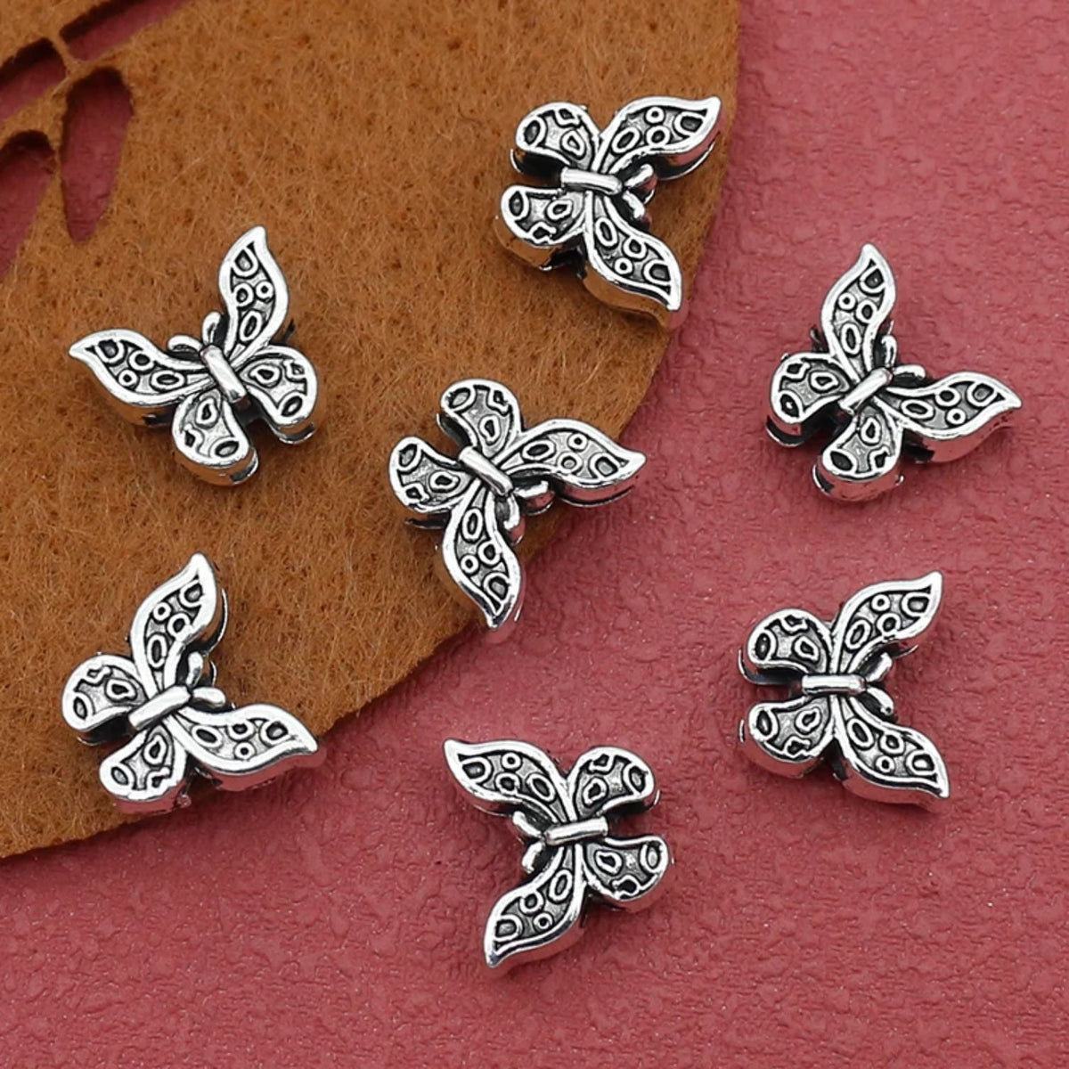 Silver-tone 10 x 12mm butterfly spacer beads on a red background