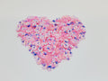 Heart-shaped pile of 6mm iridescent flower sequins in pink on a white background