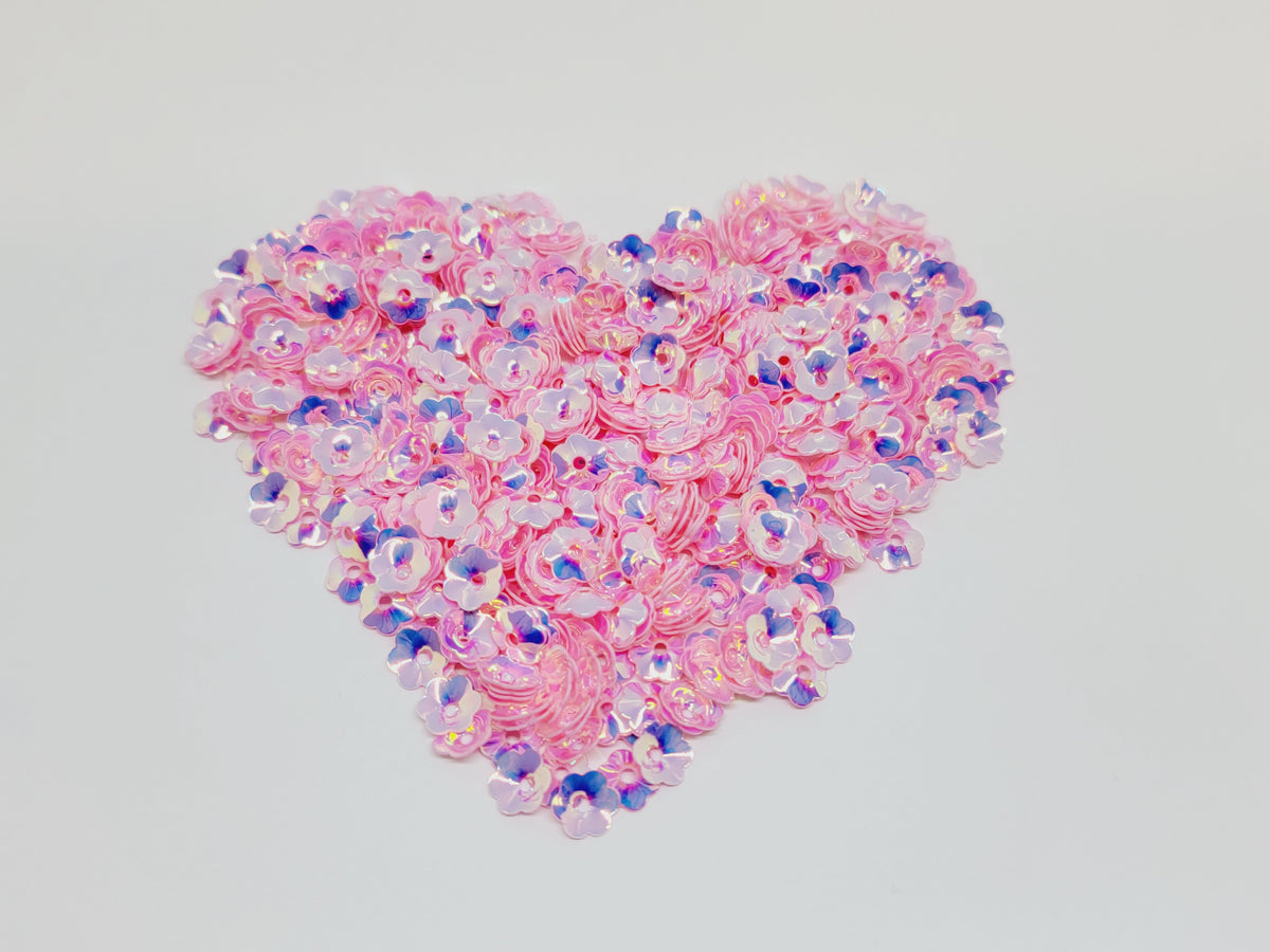 Heart-shaped pile of 6mm iridescent flower sequins in pink on a white background