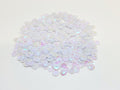 Pile of 6mm round white AB sequins with centre holes, on a white background