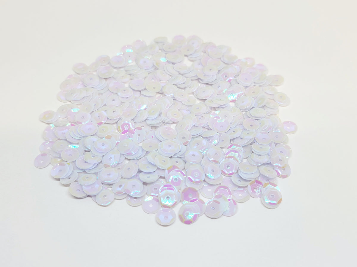 Pile of 6mm round white AB sequins with centre holes, on a white background