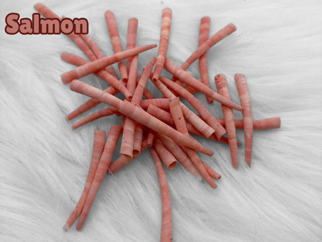 Pile of salmon dyed smooth dentalium shells, about 1.5 to 2 inches long, on white faux fur