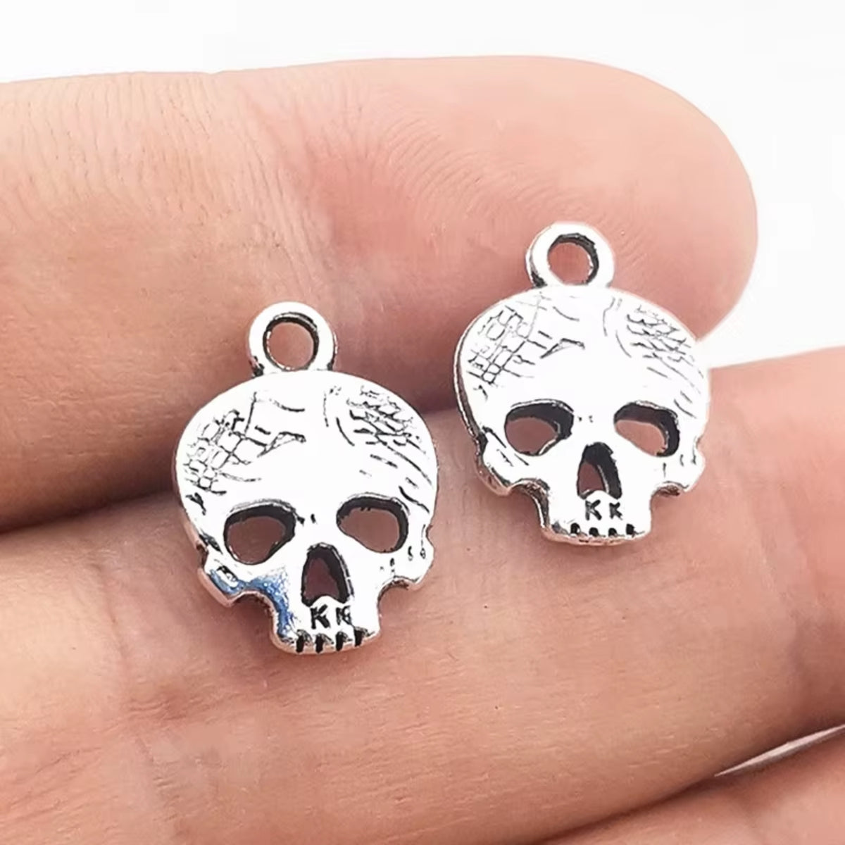 Two silver-tone 12mm skull charms with flower details held in fingers