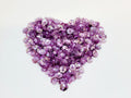 Heart-shaped pile of 6mm iridescent flower sequins in mauve on a white background