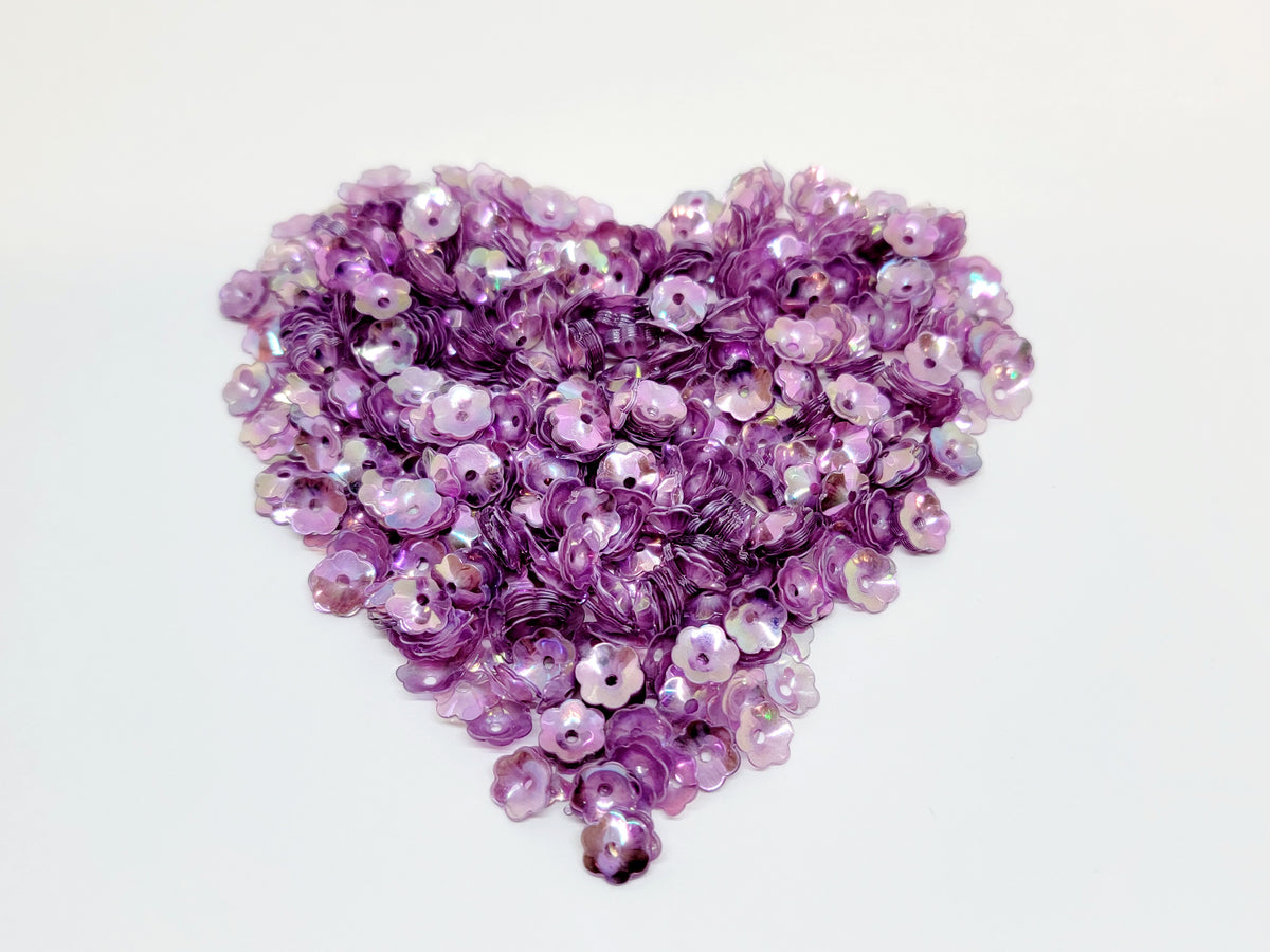 Heart-shaped pile of 6mm iridescent flower sequins in mauve on a white background