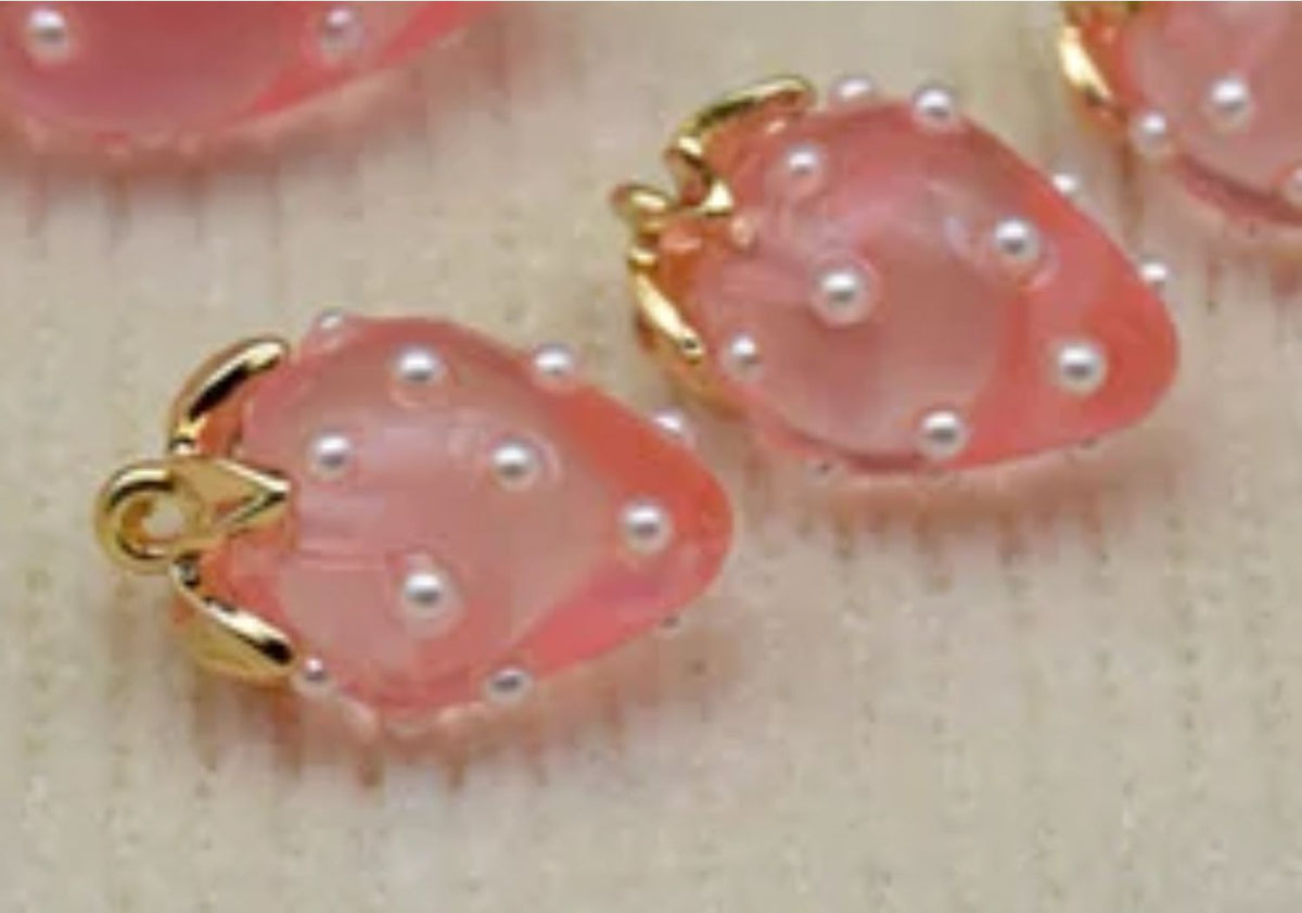 Close-up of 13 x 19mm translucent pink acrylic strawberry charms dotted with tiny pearls, with gold-tone leaf caps