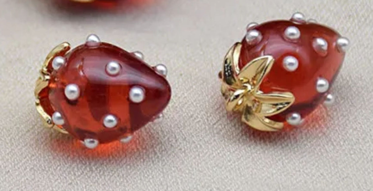 Close-up of 13 x 19mm translucent red acrylic strawberry charms dotted with tiny pearls, with gold-tone leaf caps