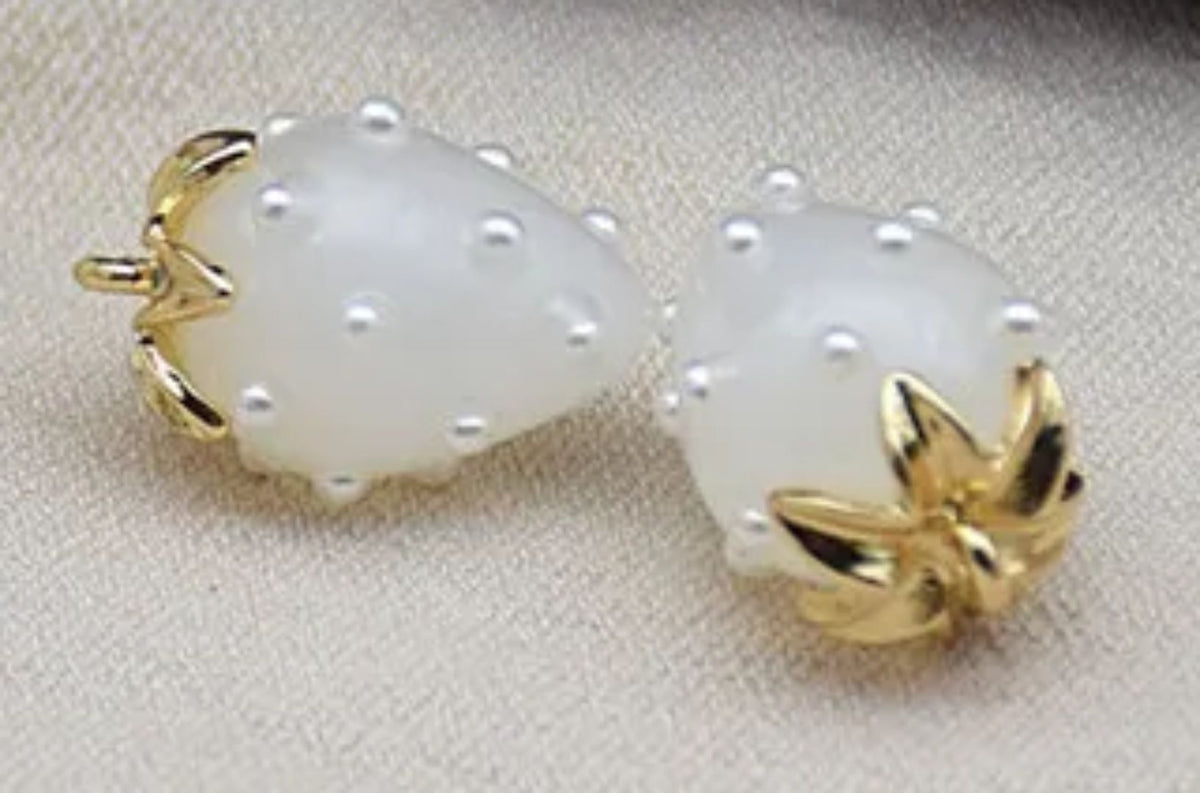 Close-up of 13 x 19mm white acrylic strawberry charms dotted with tiny pearls, with gold-tone leaf caps