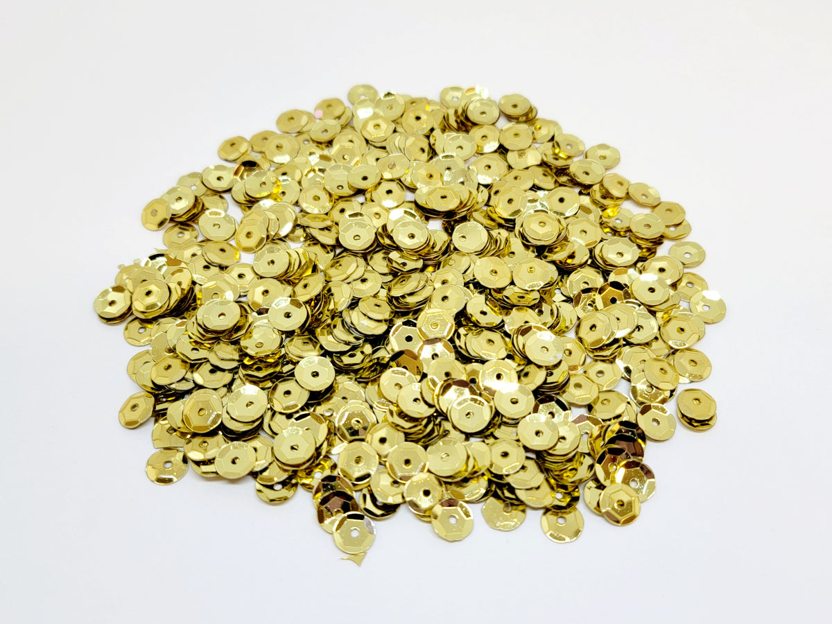 Pile of 6mm round gold sequins with centre holes, on a white background