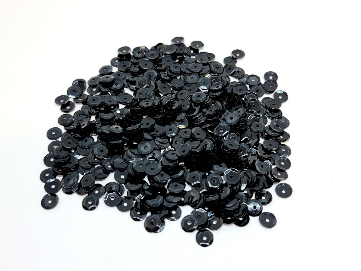 Pile of 6mm round black sequins with centre holes, on a white background