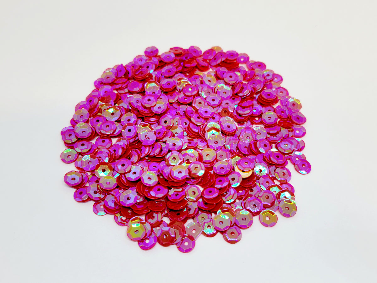 Pile of 6mm round red sequins with centre holes, on a white background