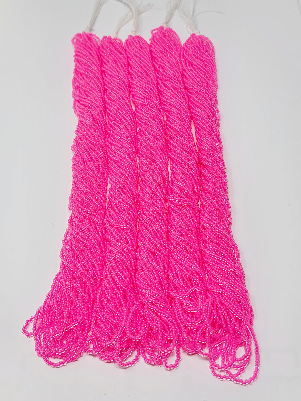 Five hanks of Preciosa 11/0 transparent neon pink seed beads laid out on a white background