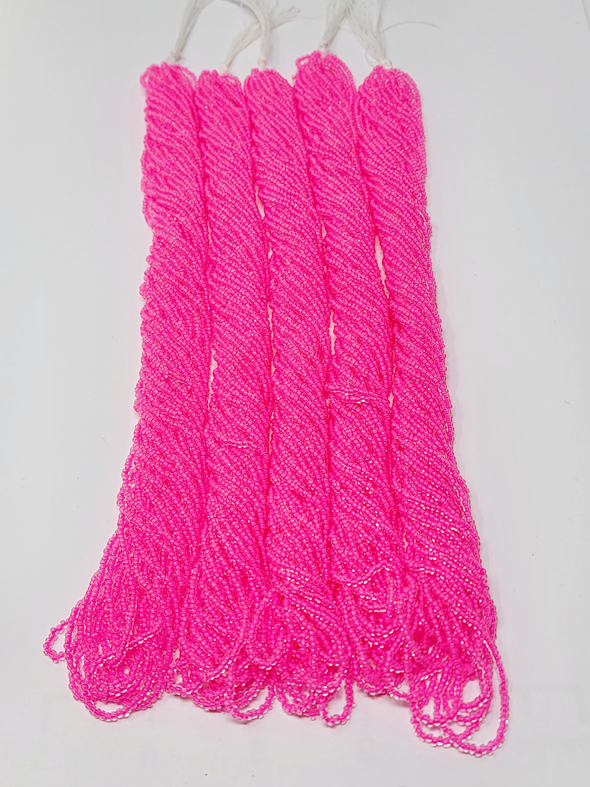 Five hanks of Preciosa 11/0 transparent neon pink seed beads laid out on a white background