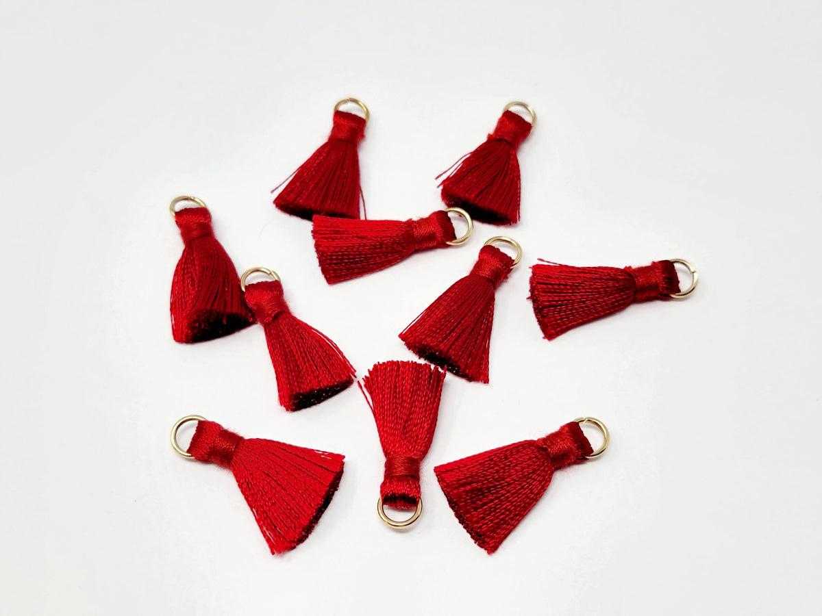Scattered 2.5cm red cotton tassels with gold-tone jump rings on a white background