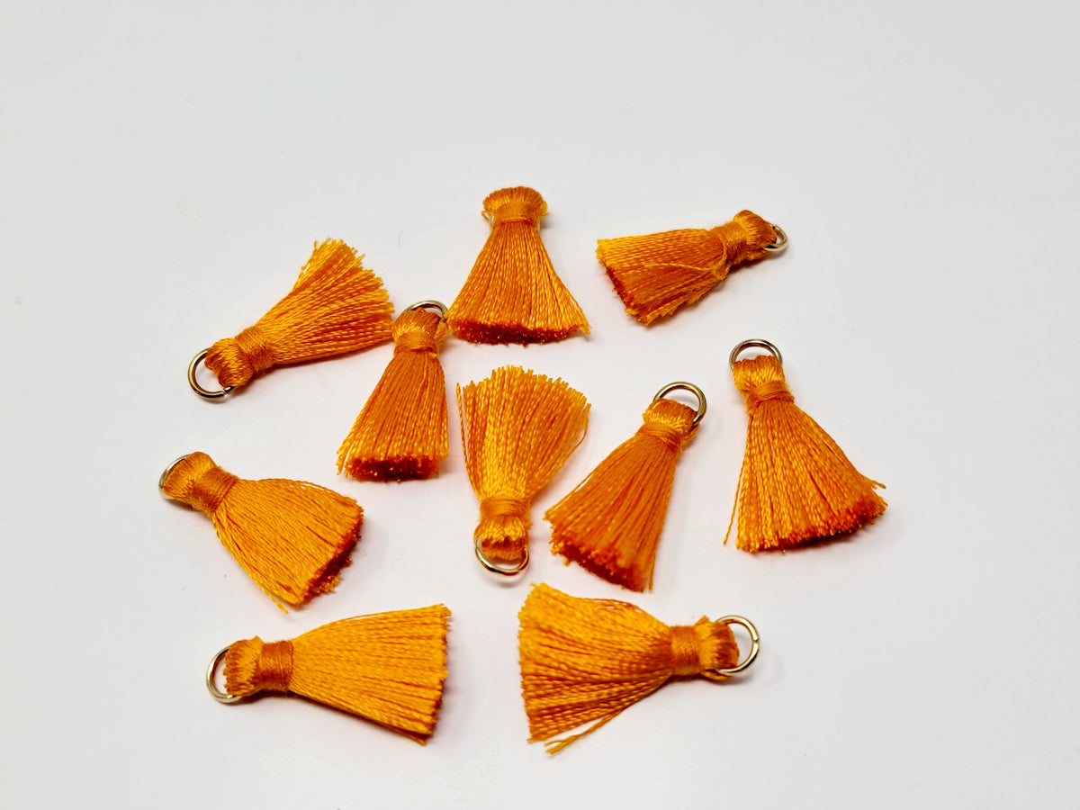 Scattered 2.5cm orange cotton tassels with gold-tone jump rings on a white background
