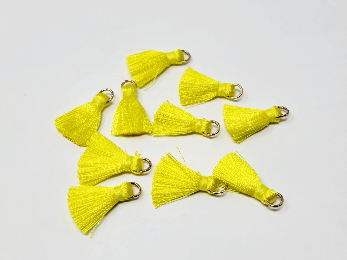 Scattered 2.5cm yellow cotton tassels with gold-tone jump rings on a white background
