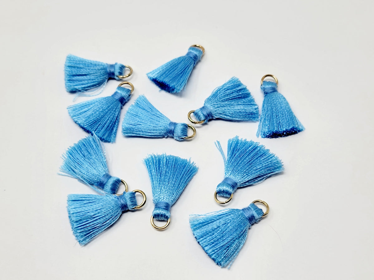 Scattered 2.5cm blue cotton tassels with gold-tone jump rings on a white background