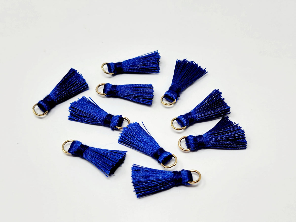 Scattered 2.5cm cobalt cotton tassels with gold-tone jump rings on a white background