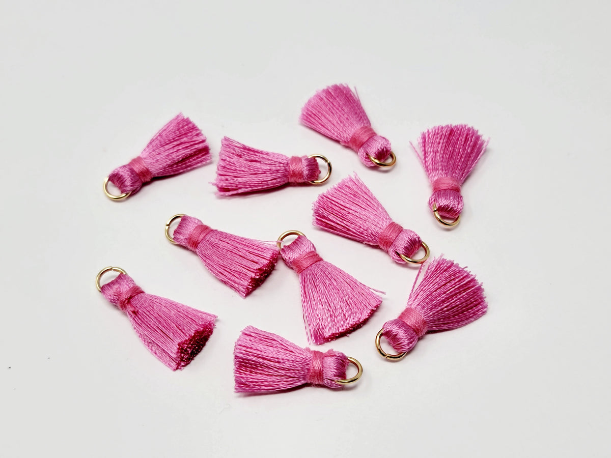 Scattered 2.5cm pink cotton tassels with gold-tone jump rings on a white background