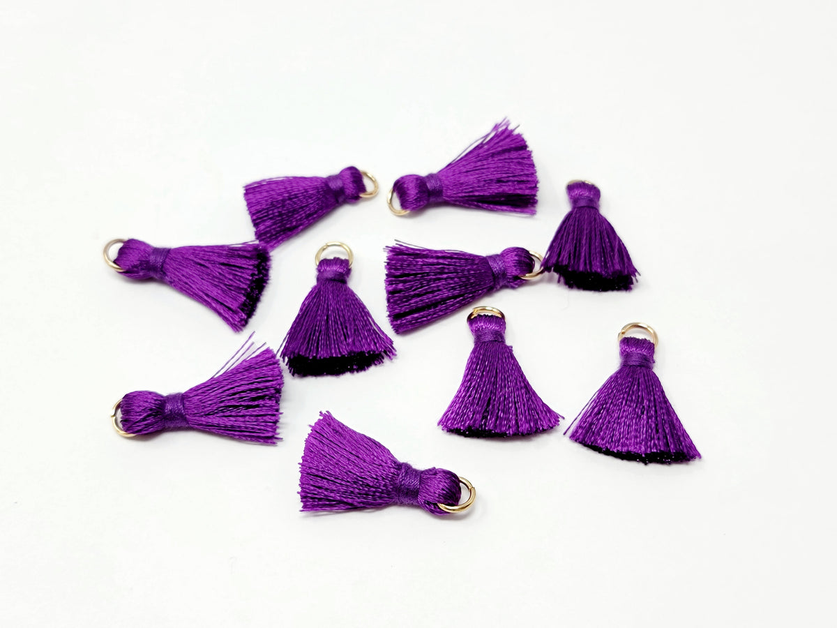 Scattered 2.5cm purple cotton tassels with gold-tone jump rings on a white background