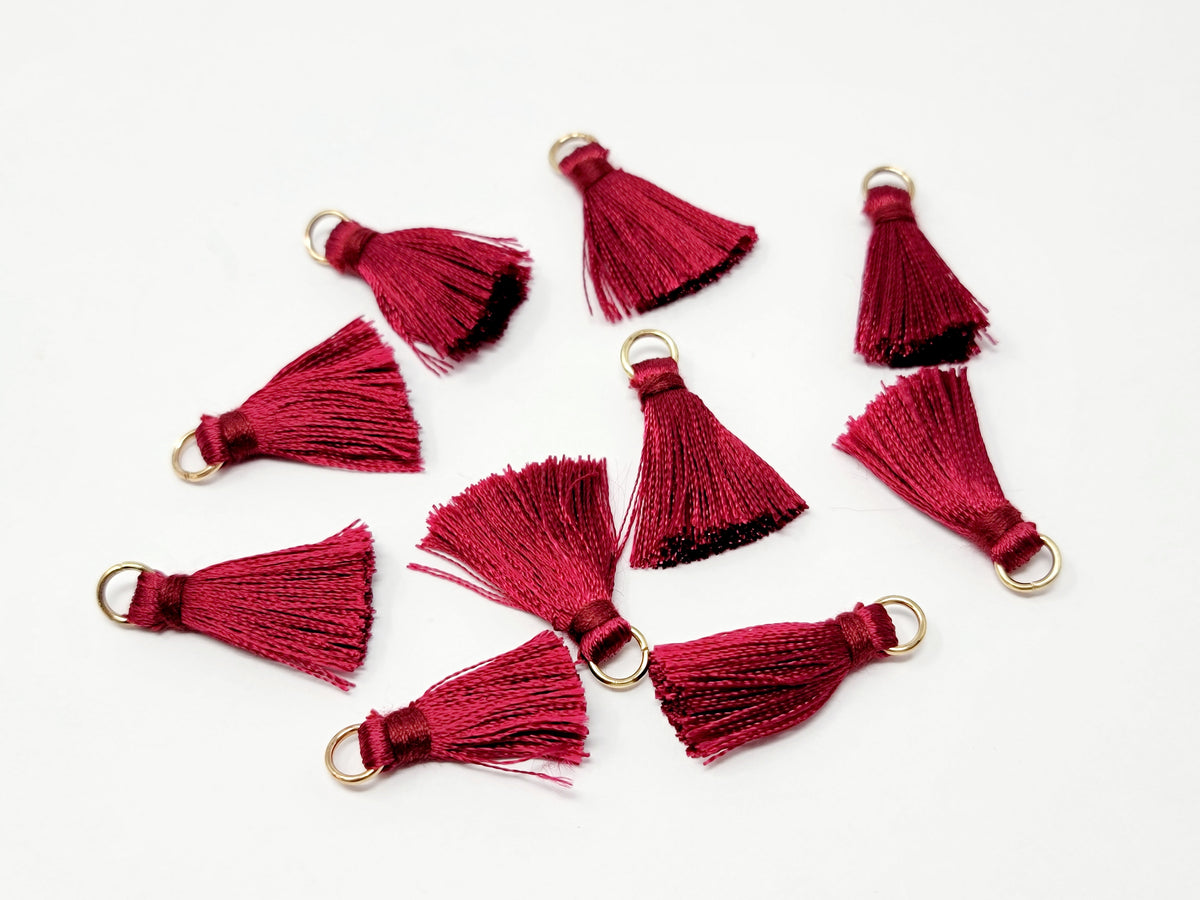 Scattered 2.5cm maroon cotton tassels with gold-tone jump rings on a white background