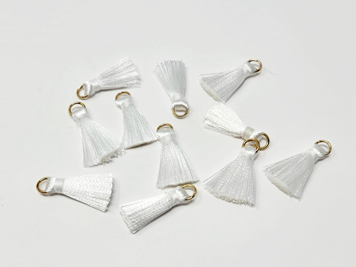 Scattered 2.5cm white cotton tassels with gold-tone jump rings on a white background