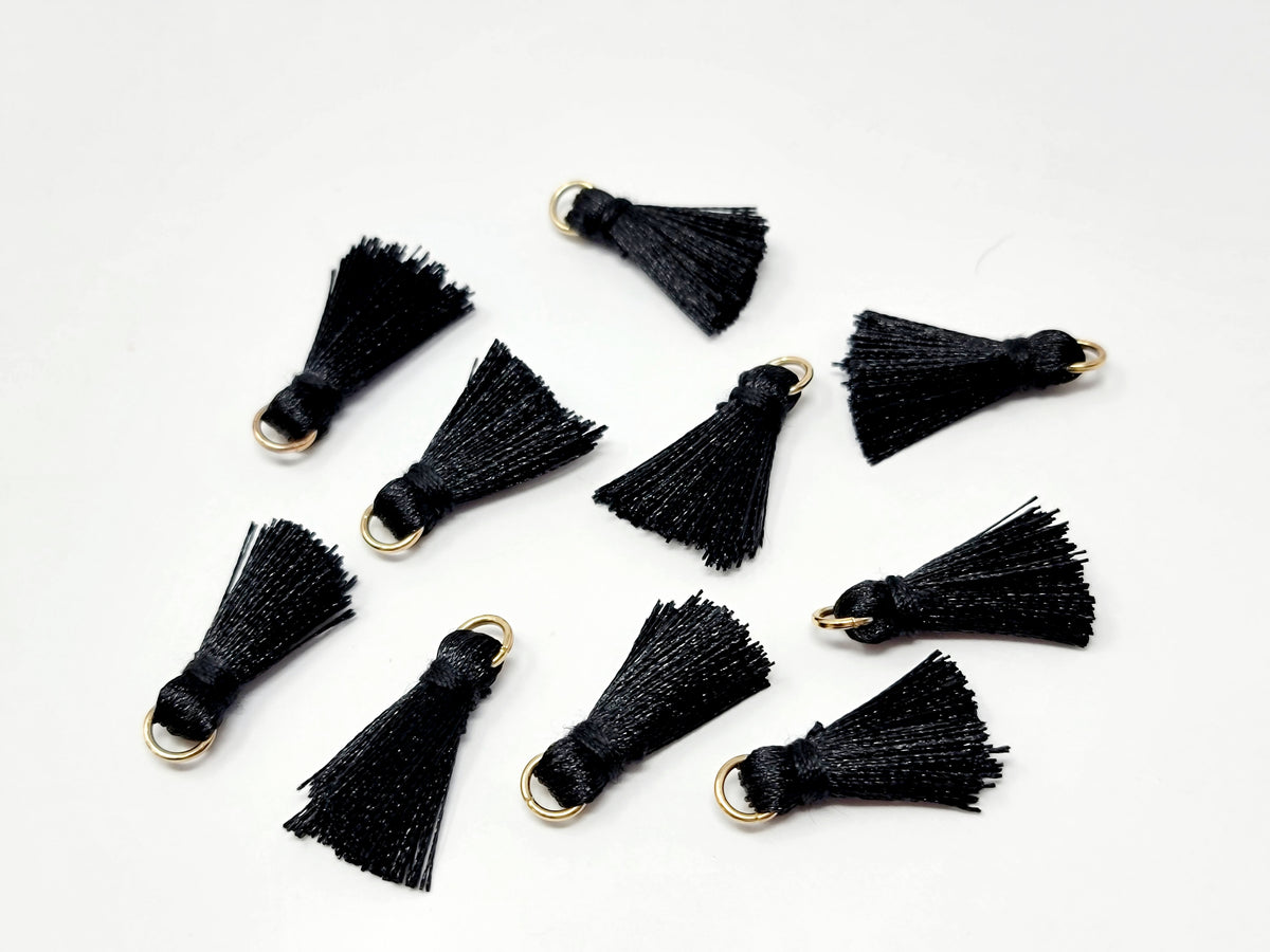 Scattered 2.5cm black cotton tassels with gold-tone jump rings on a white background