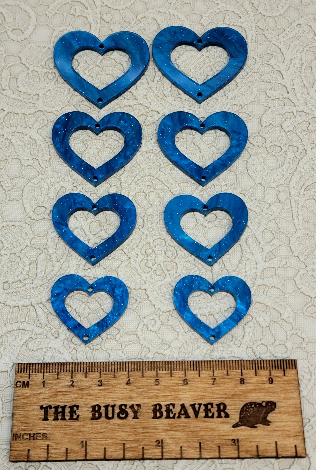 Two sets of four graduated acrylic open hearts in blue ripple with glitter, beside a ruler