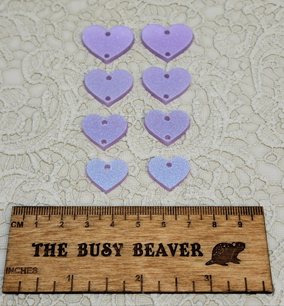 Two sets of four graduated acrylic hearts in iridescent light purple, beside a ruler