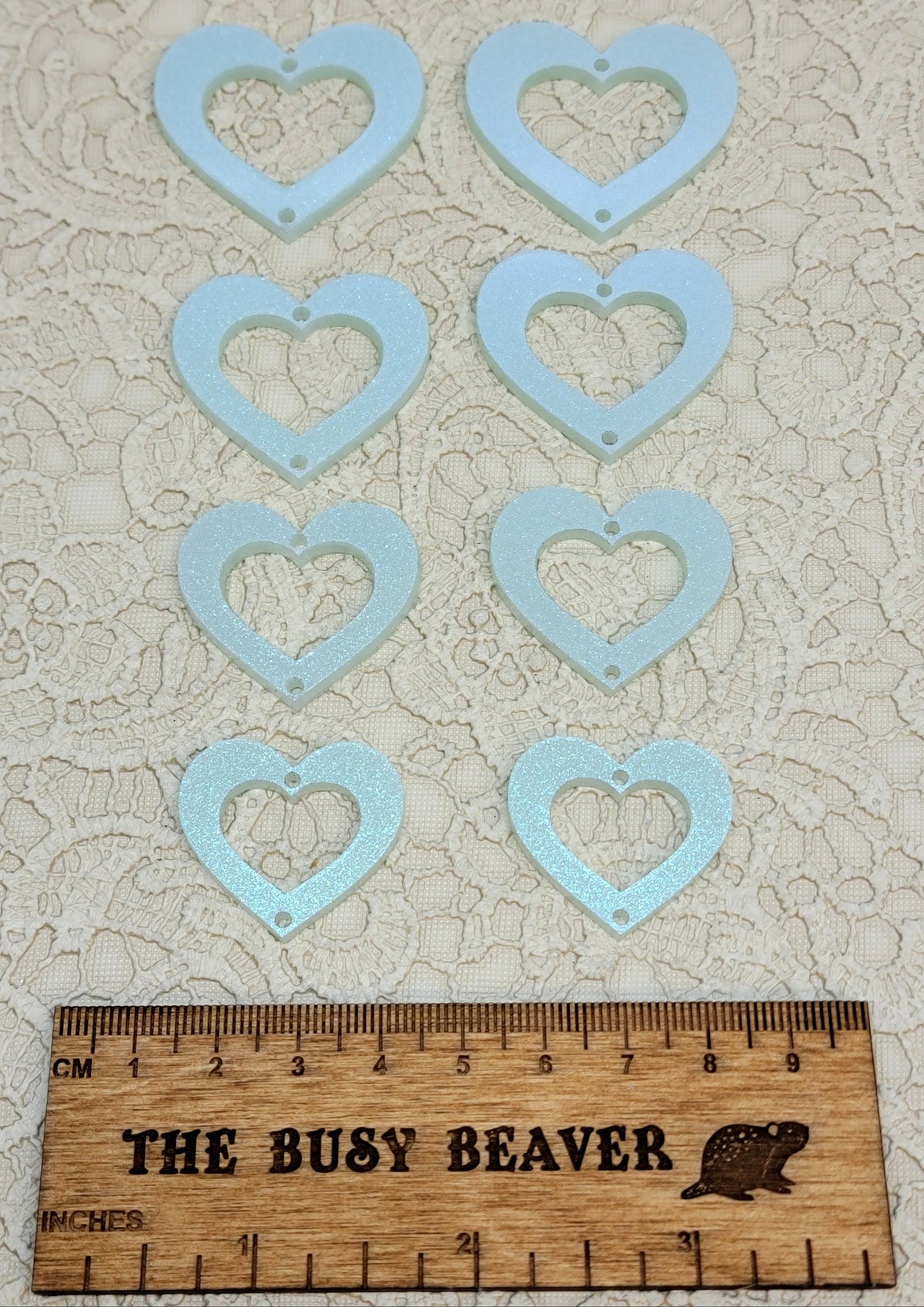 Two sets of four graduated acrylic open hearts in iridescent icy blue, beside a ruler
