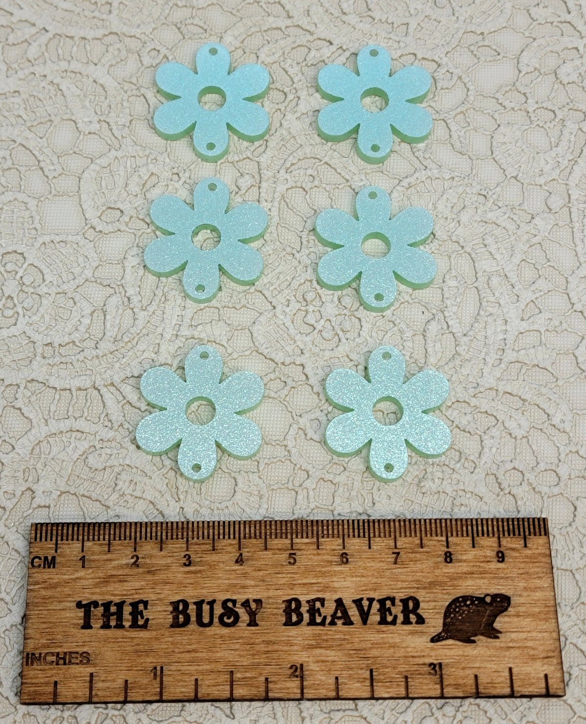 Two sets of three graduated acrylic flower pieces in iridescent light green, beside a ruler