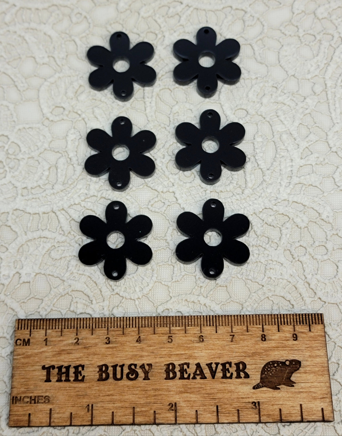 Two sets of three graduated acrylic flower pieces in black, beside a ruler