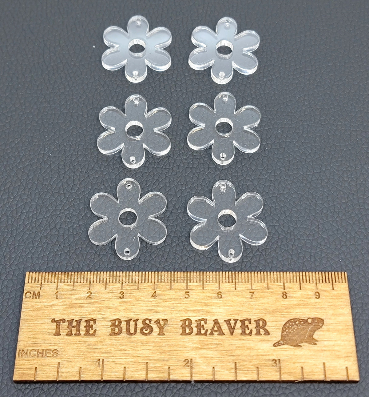 Two sets of three graduated acrylic flower pieces in clear, beside a ruler