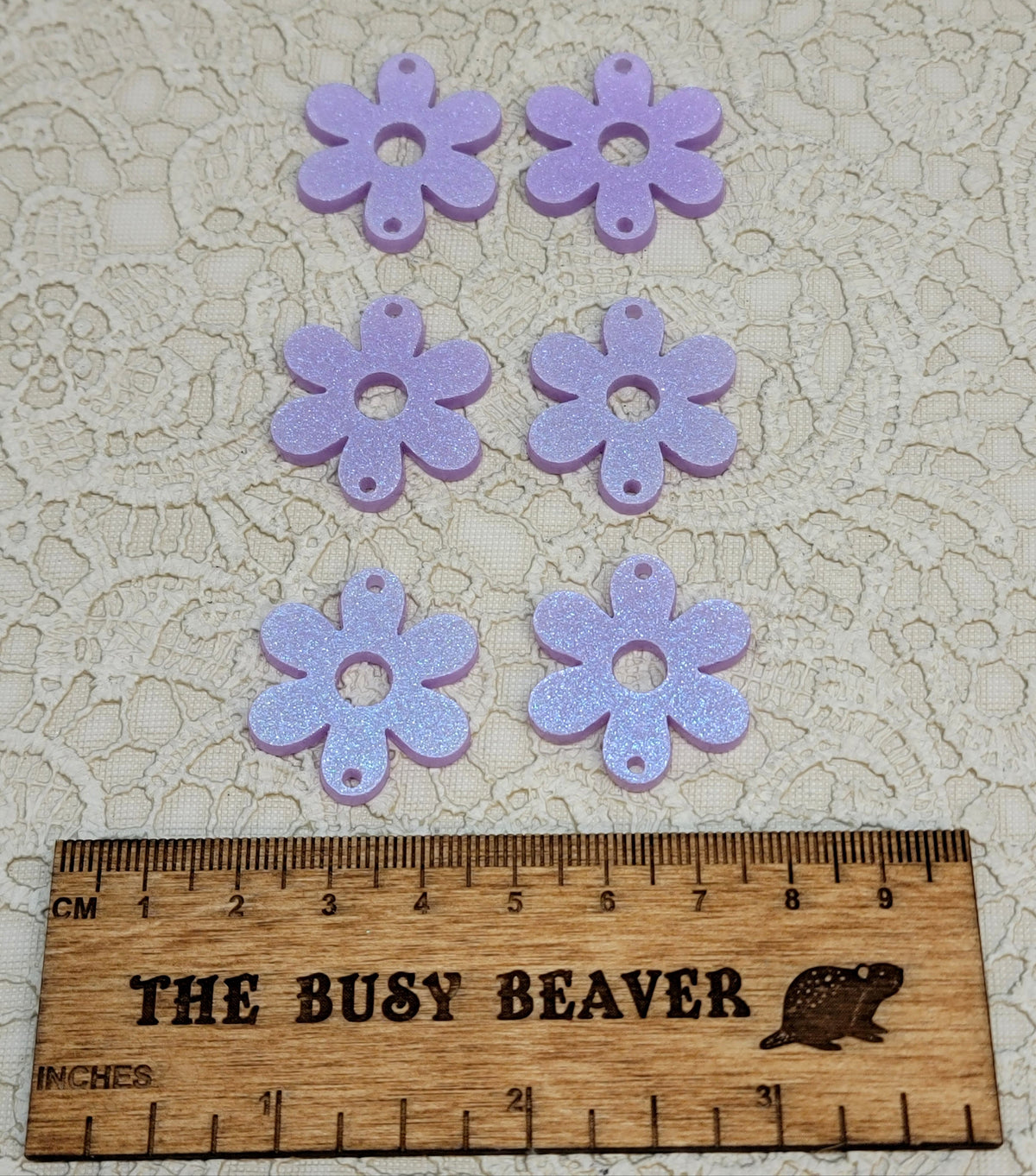 Two sets of three graduated acrylic flower pieces in iridescent light purple, beside a ruler