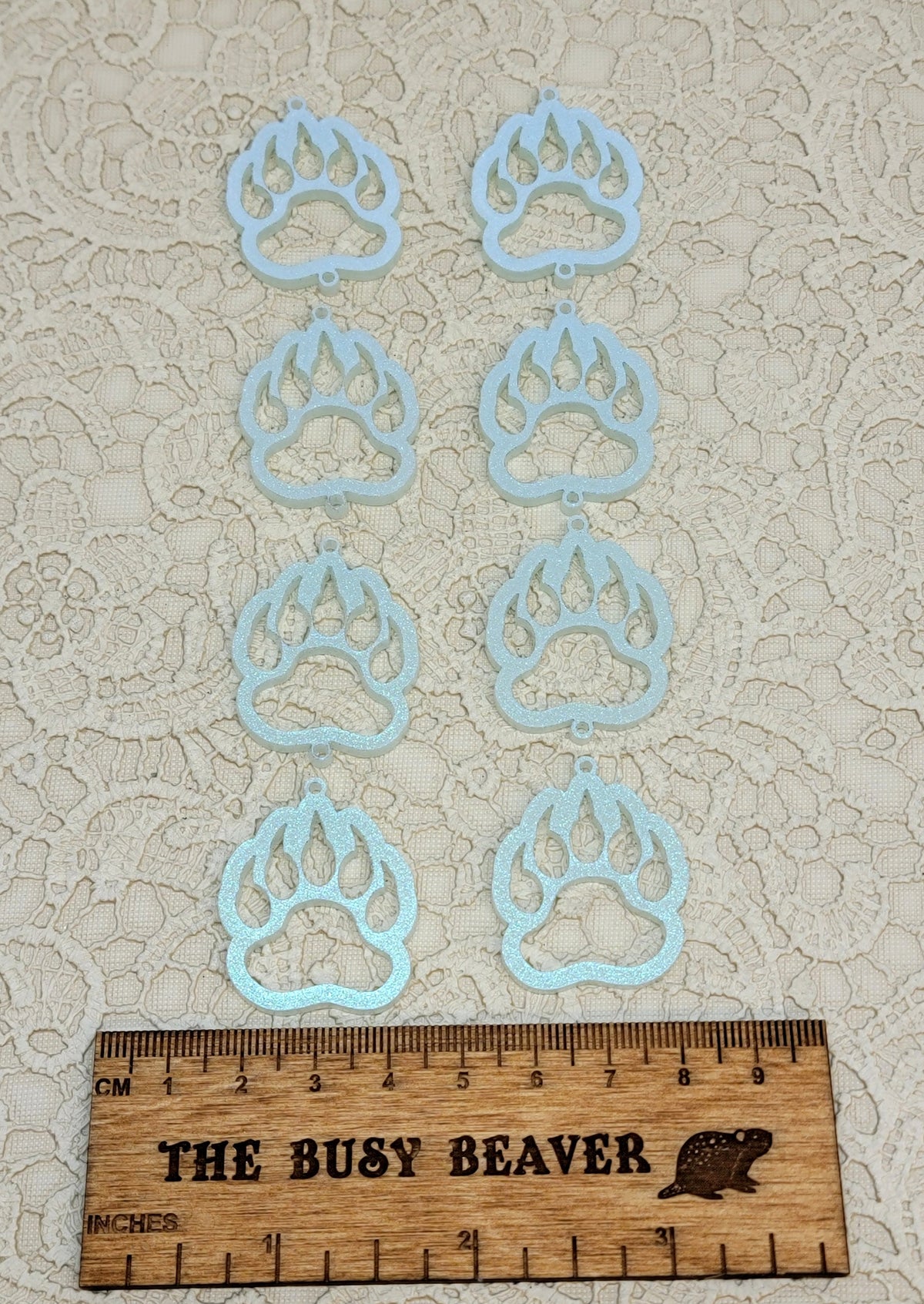 Two sets of four graduated acrylic open bear paws in iridescent icy blue, beside a ruler