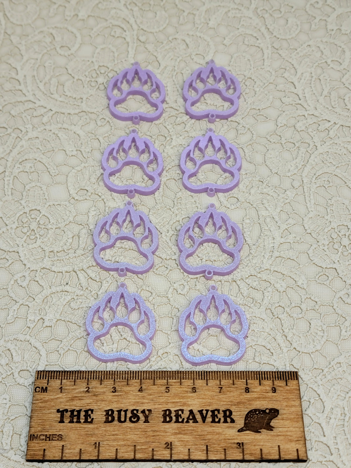 Two sets of four graduated acrylic open bear paws in iridescent light purple, beside a ruler