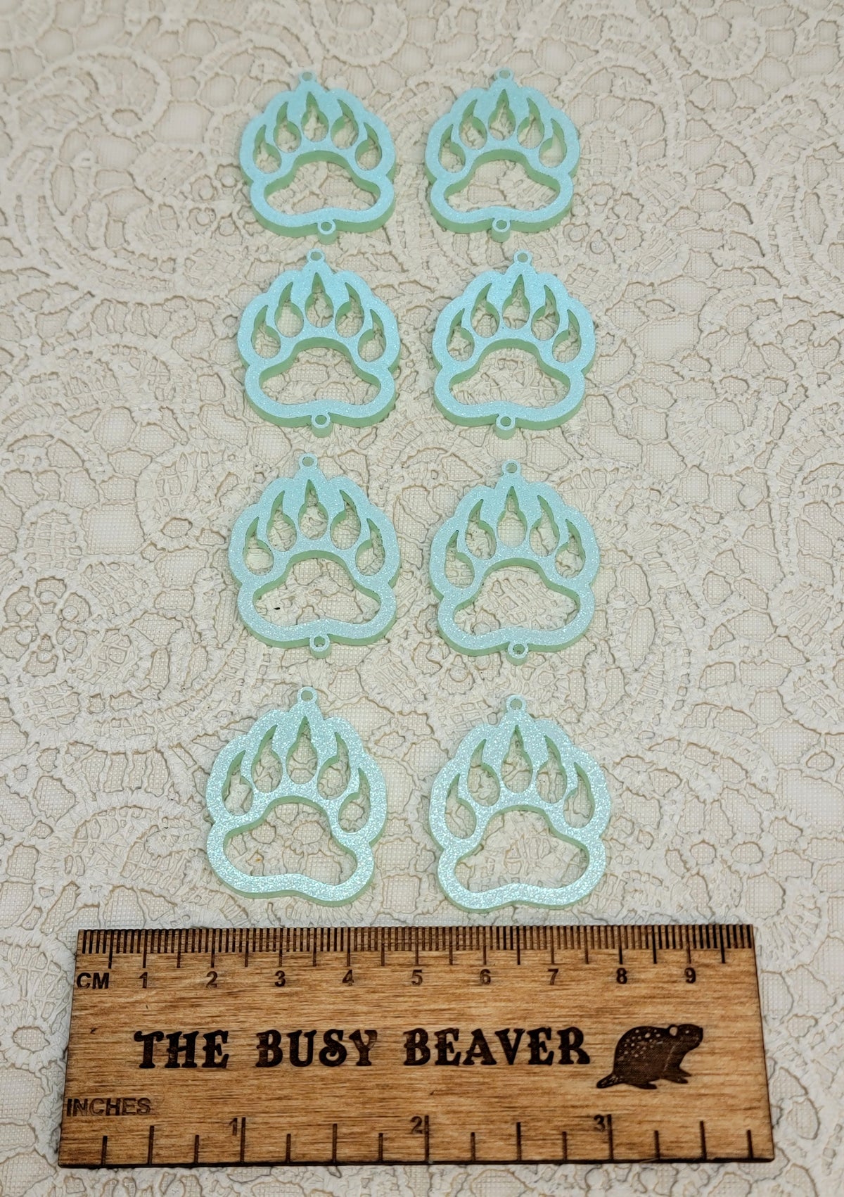 Two sets of four graduated acrylic open bear paws in iridescent light green, beside a ruler