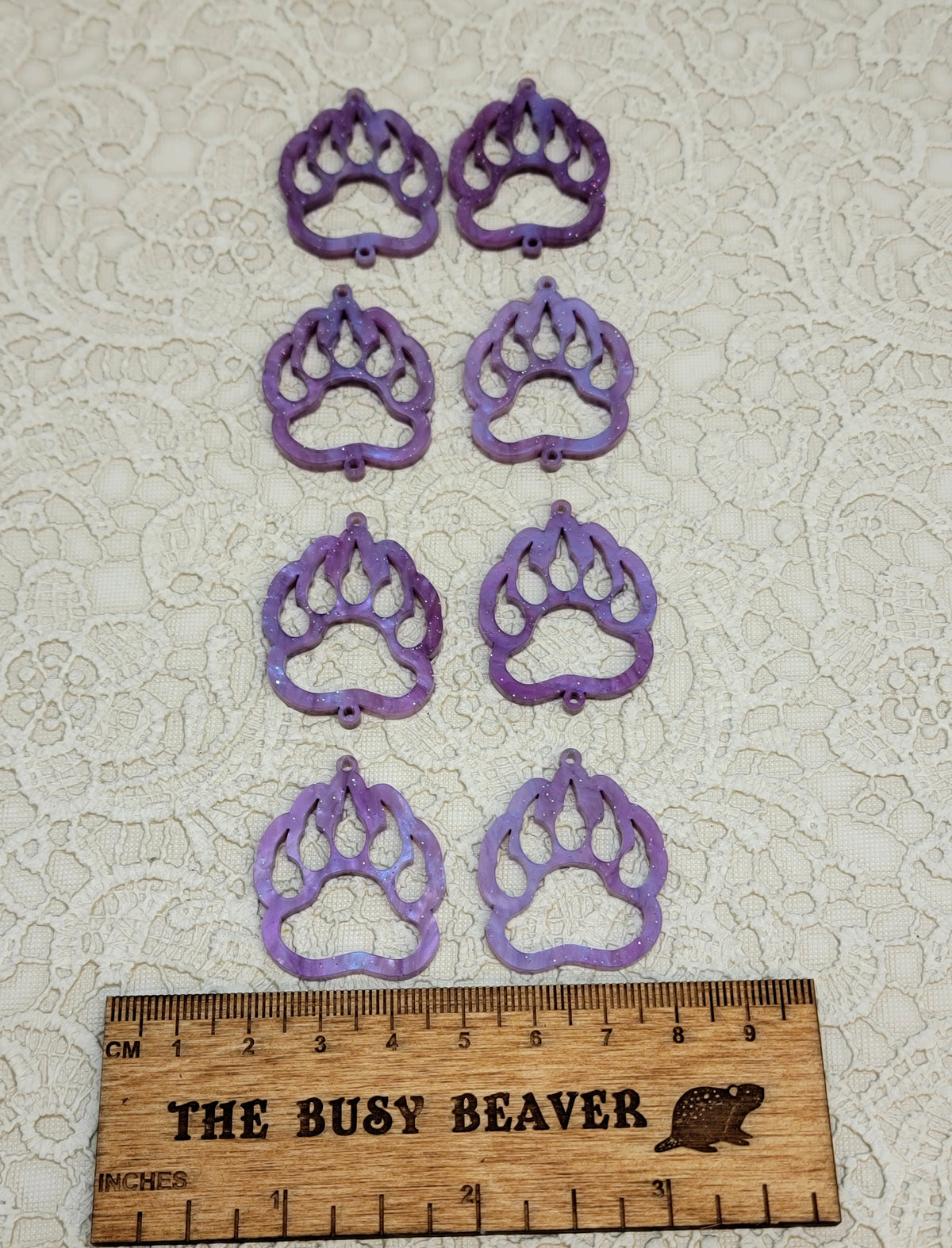 Two sets of four graduated acrylic open bear paws in purple ripple with glitter, beside a ruler