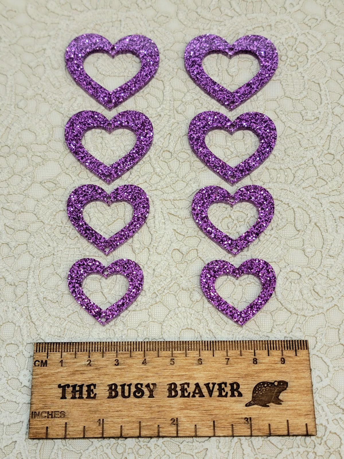 Two sets of four graduated acrylic open hearts in purple glitter, beside a ruler