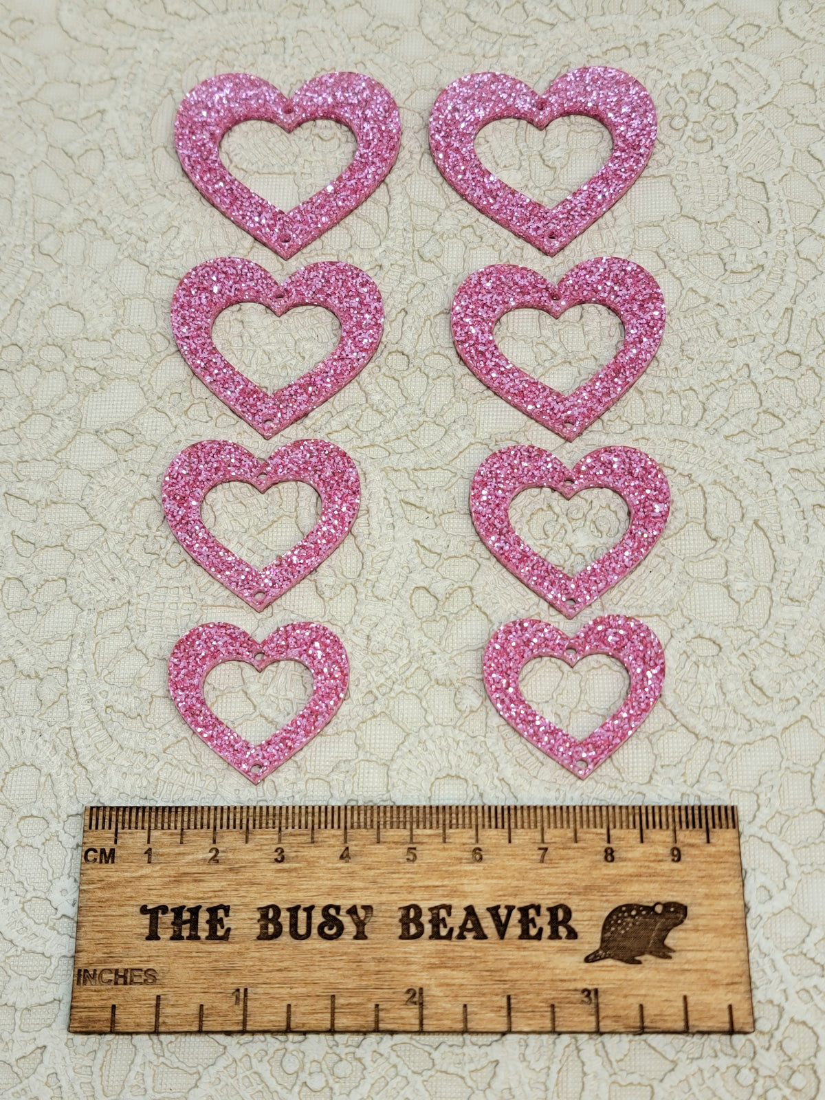 Two sets of four graduated acrylic open hearts in pink glitter, beside a ruler