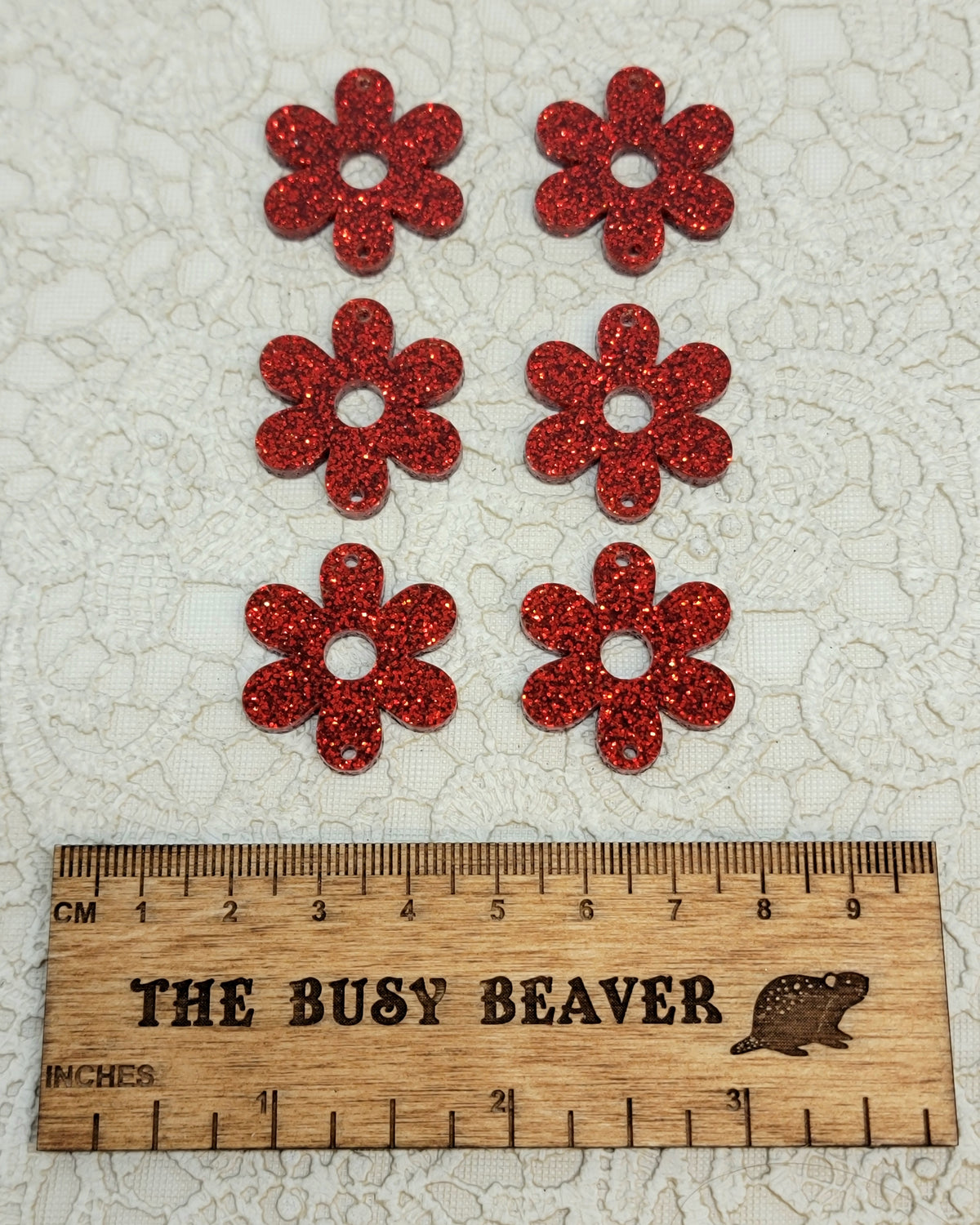 Two sets of three graduated acrylic flower pieces in red glitter, beside a ruler