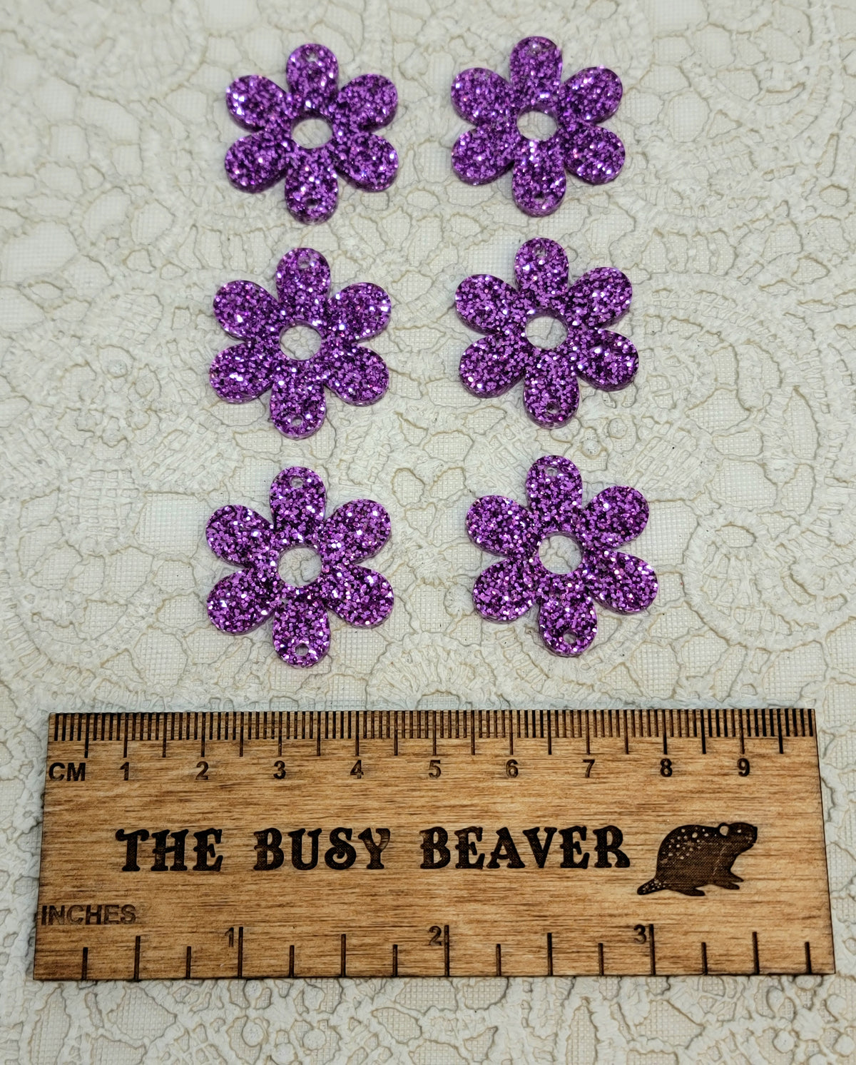 Two sets of three graduated acrylic flower pieces in purple glitter, beside a ruler