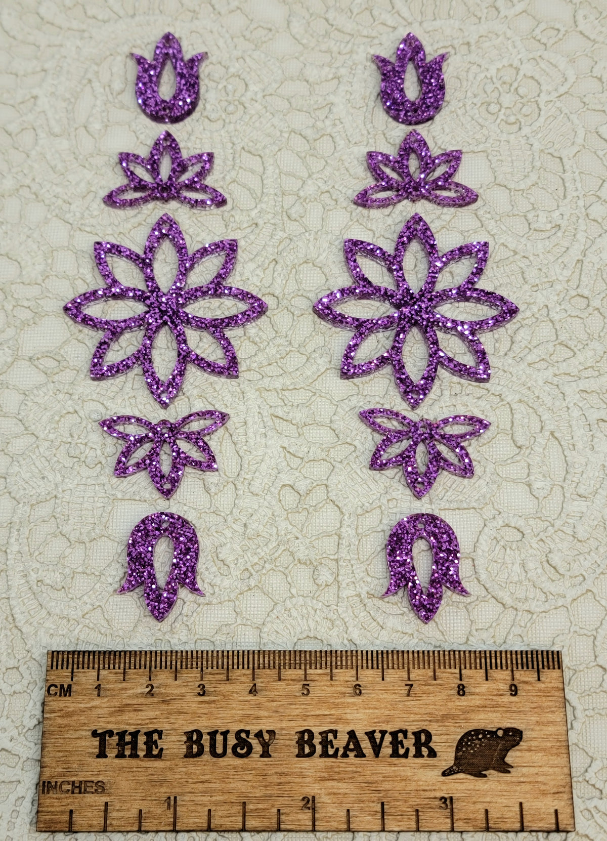 Two 5-tier acrylic flower earring sets in purple glitter, laid out top to bottom beside a ruler